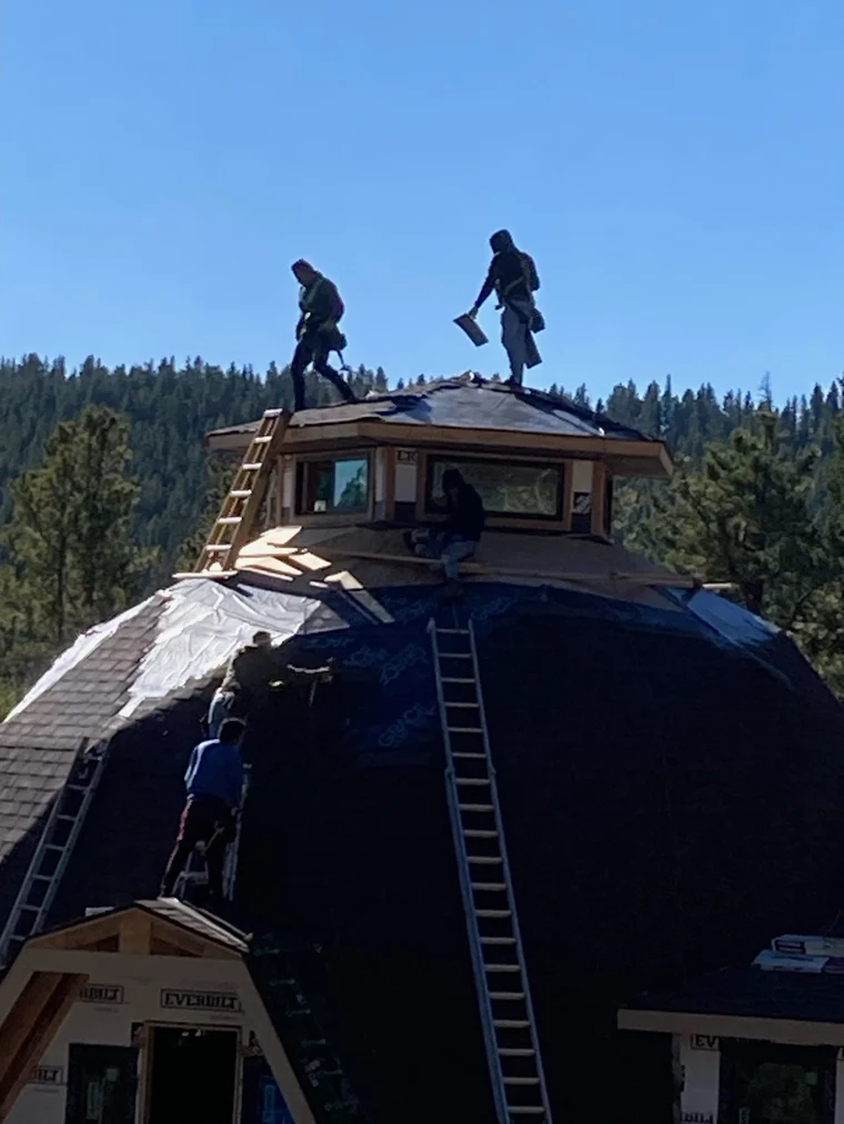 Roofers working on top of a dome-shaped roof against a blue sky