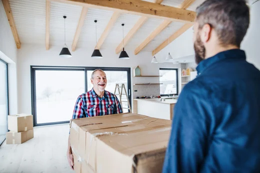 Smiling older man carrying a moving box into a bright kitchen